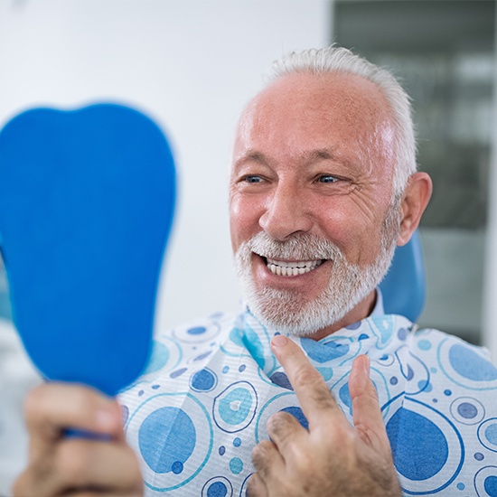 Man checking smile in blue mirror after dental implant tooth replacement
