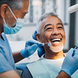 Dentist in blue scrubs examining a patient with gray hair