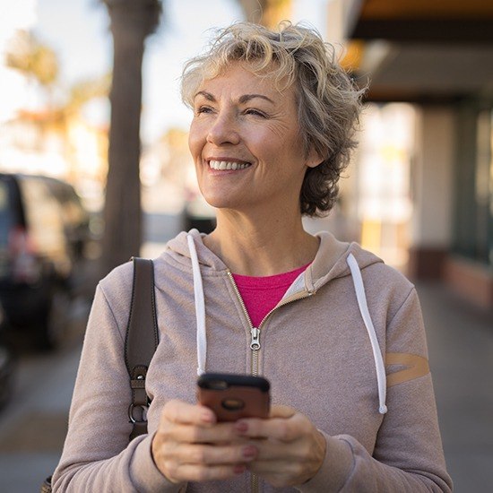Woman outside on cell phone smiling after one visit dental restoration