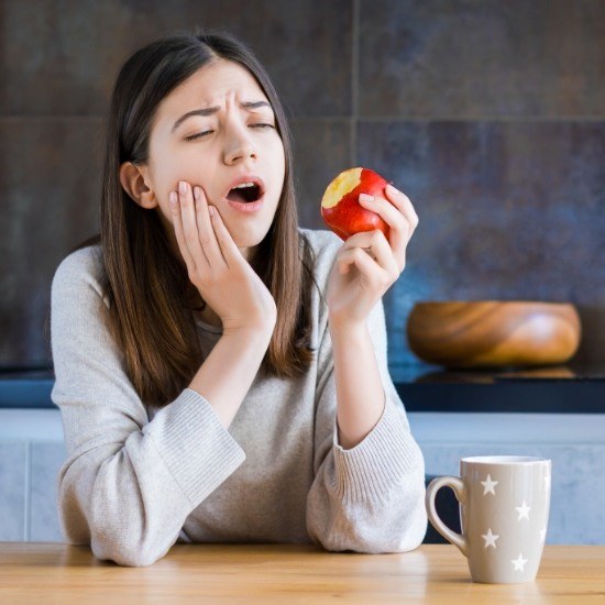 Woman in pain holding apple before emergency dentistry