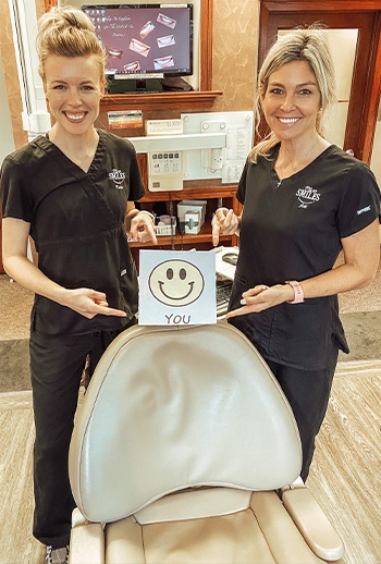 Two smiling Covington dental team members next to dental chair
