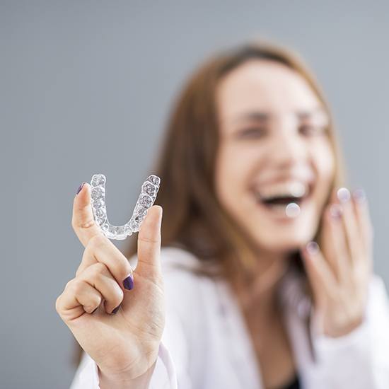 Woman laughing and holding Invisalign aligner