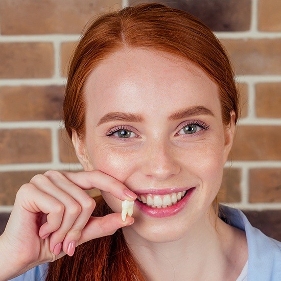 Woman holding tooth and smiling after tooth extraction
