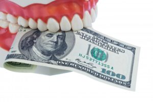 A pair of dentures holding a one hundred-dollar bill.