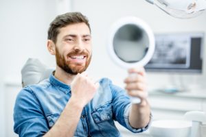 man admiring the cosmetic benefits of dental implants in his smile in the mirror 