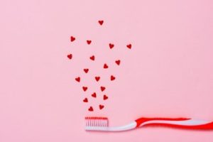 Small red hearts floating above the bristles of a red and white toothbrush against a pink background